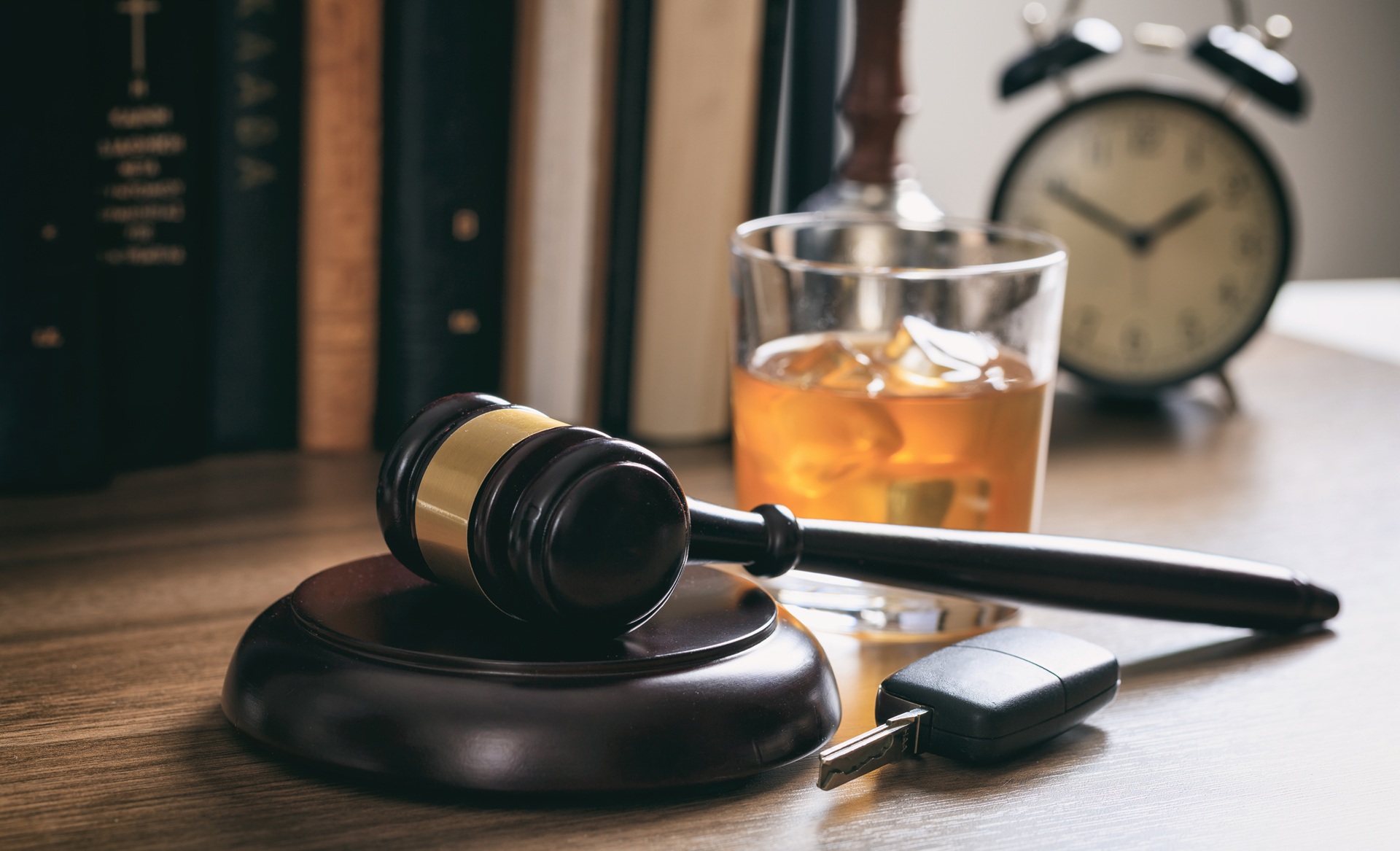 A gavel rests on its stand next to a glass of alcohol and keys to a car.